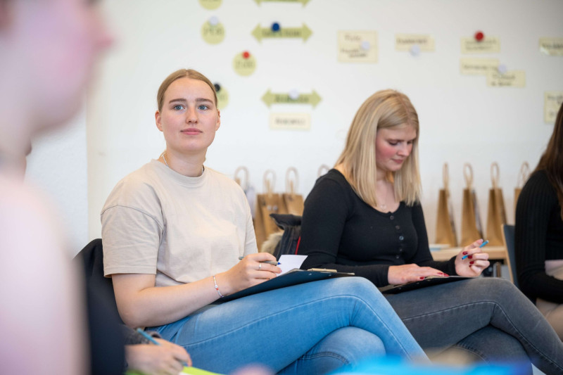 Zwei junge Frauen sitzen in einem Seminarraum und machen sich Notizen