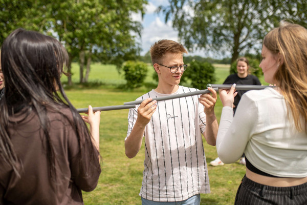 Junge Menschen balancieren bei einem Gruppenspiel im Freien gemeinsam einen Stab