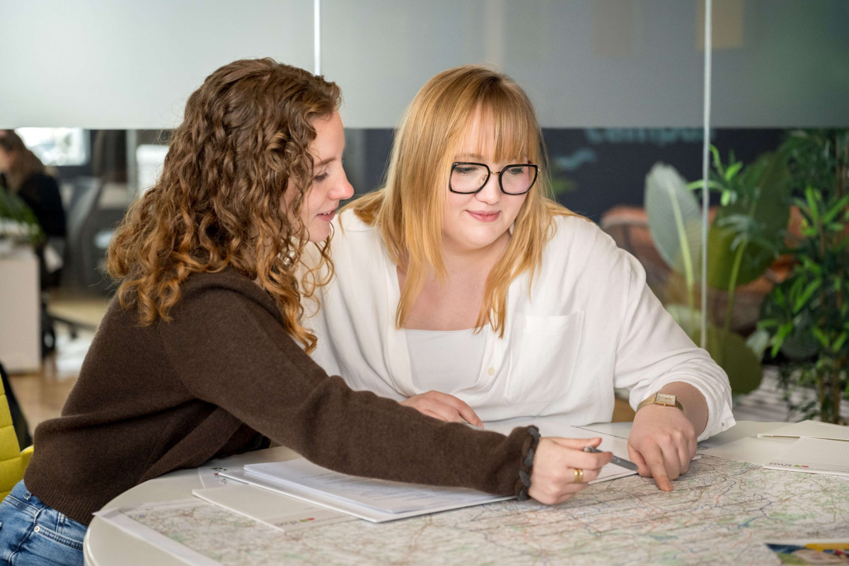 Zwei junge Frauen besprechen gemeinsam Unterlagen an einem Tisch